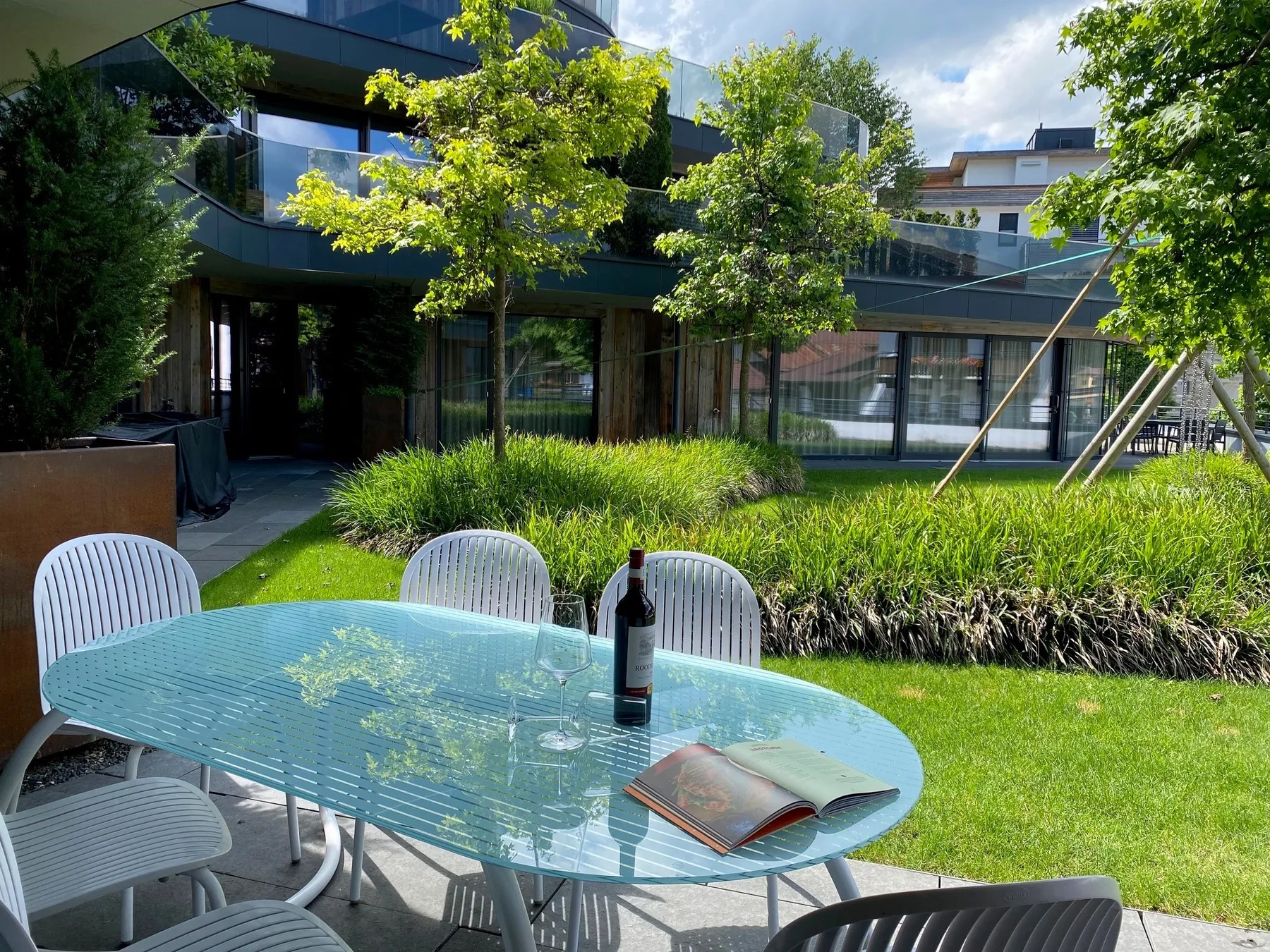 Una mesa de patio de vidrio y asientos están sobre el césped junto a un edificio moderno.