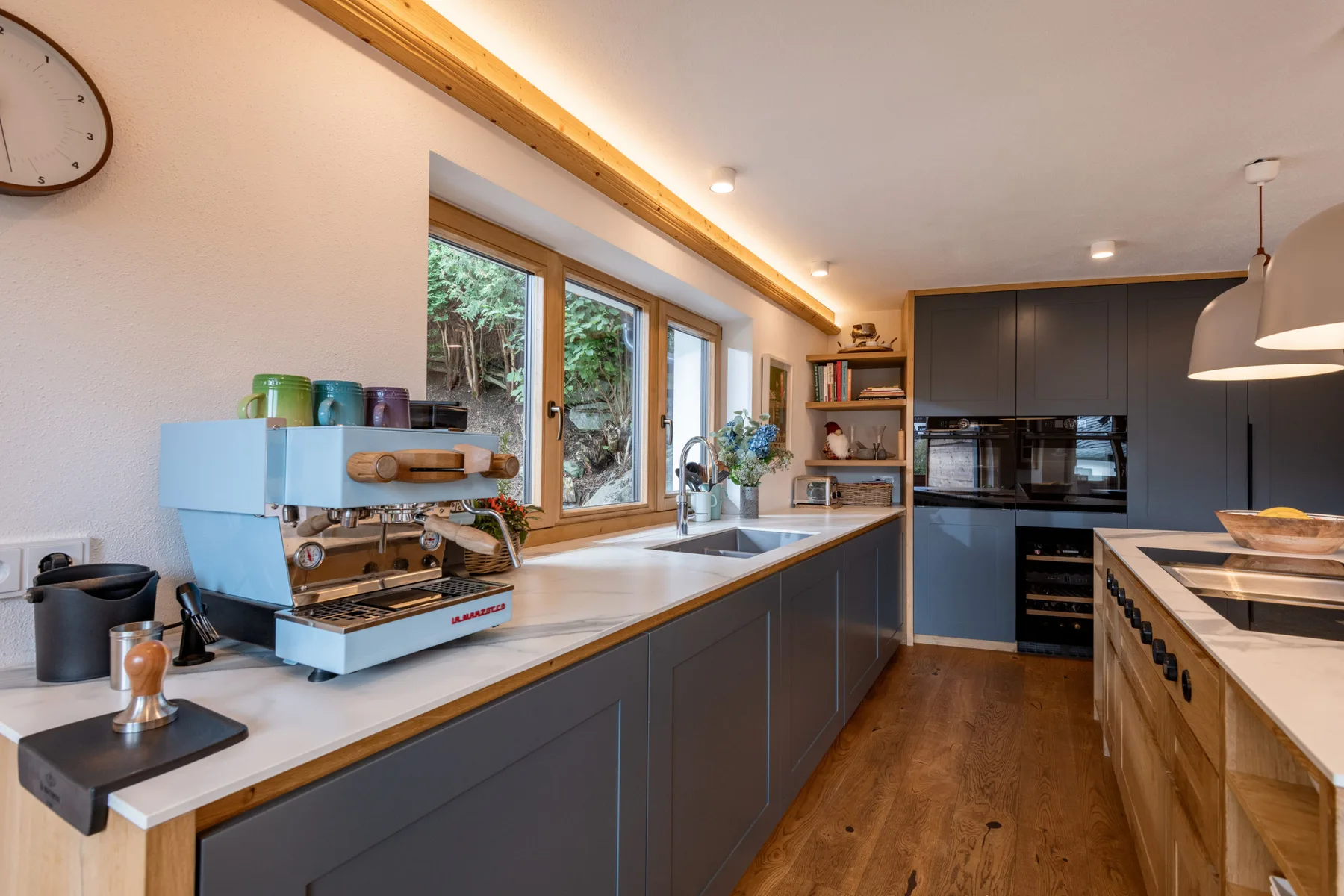 Una cocina moderna con gabinetes oscuros, encimeras de madera y grandes ventanas.