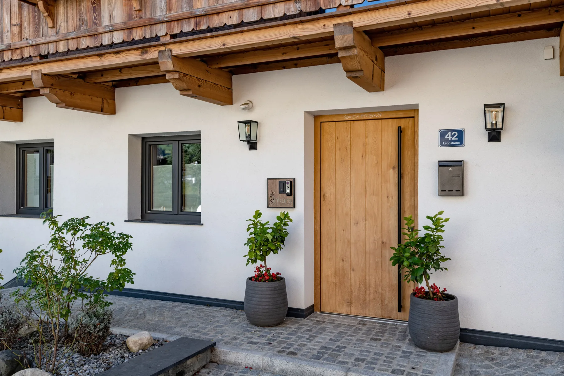 La entrada de un edificio con una puerta de madera, ventanas y plantas en macetas.