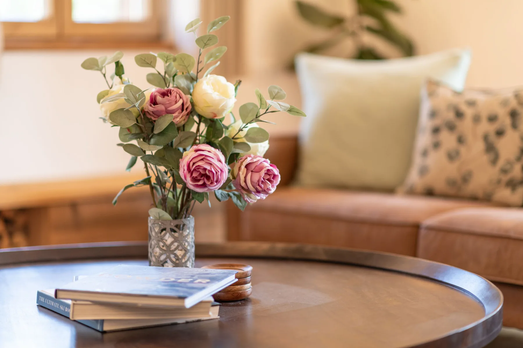 Una zona de estar con una mesa redonda que sostiene libros y un florero con flores.