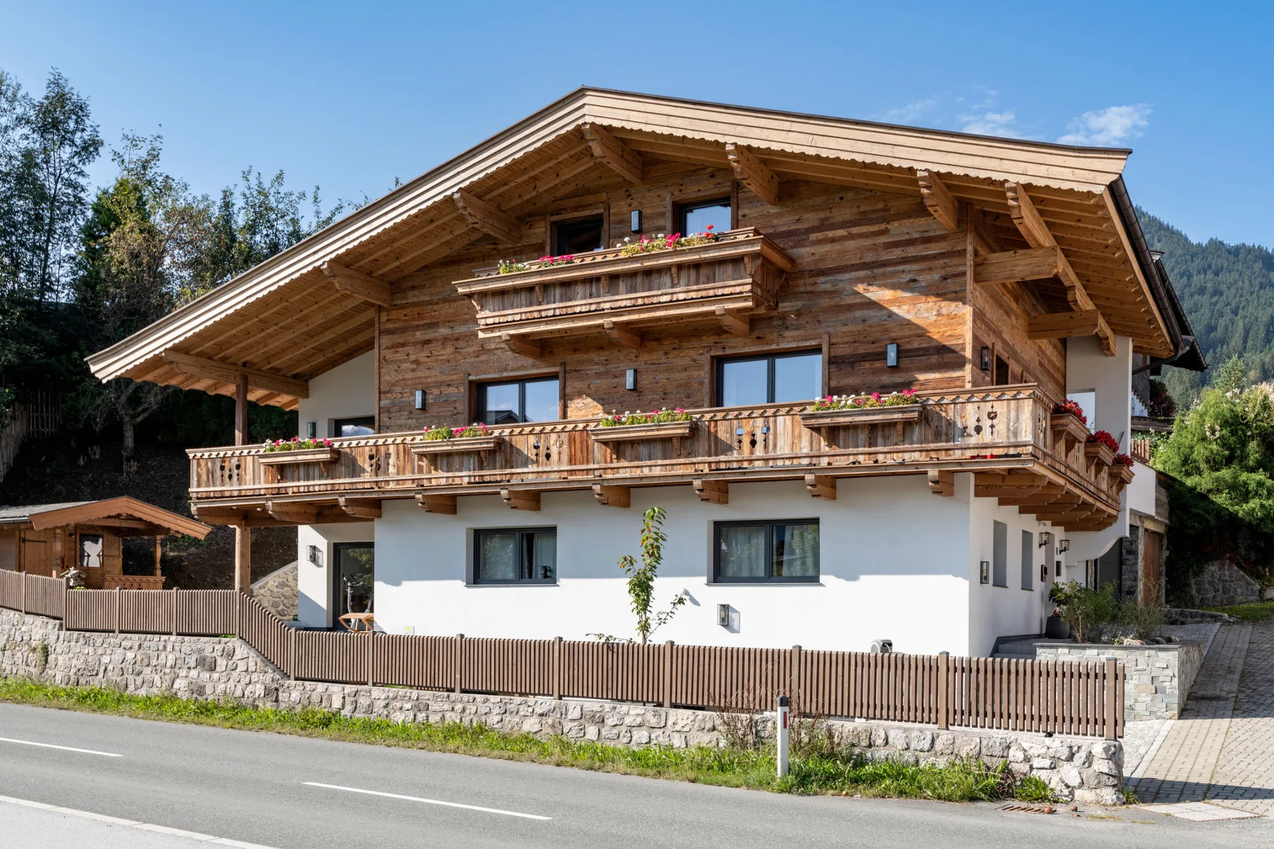 Una casa grande de estilo chalet con balcones de madera está junto a una carretera pavimentada.