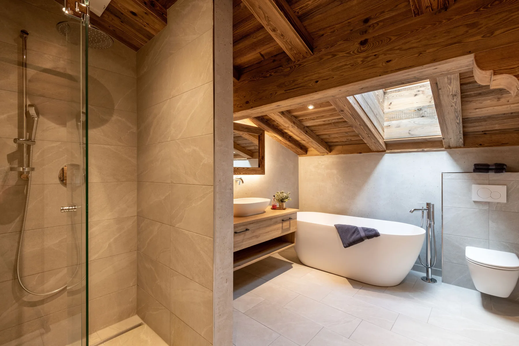 Un baño con bañera exenta, ducha y claraboya bajo un techo de madera.