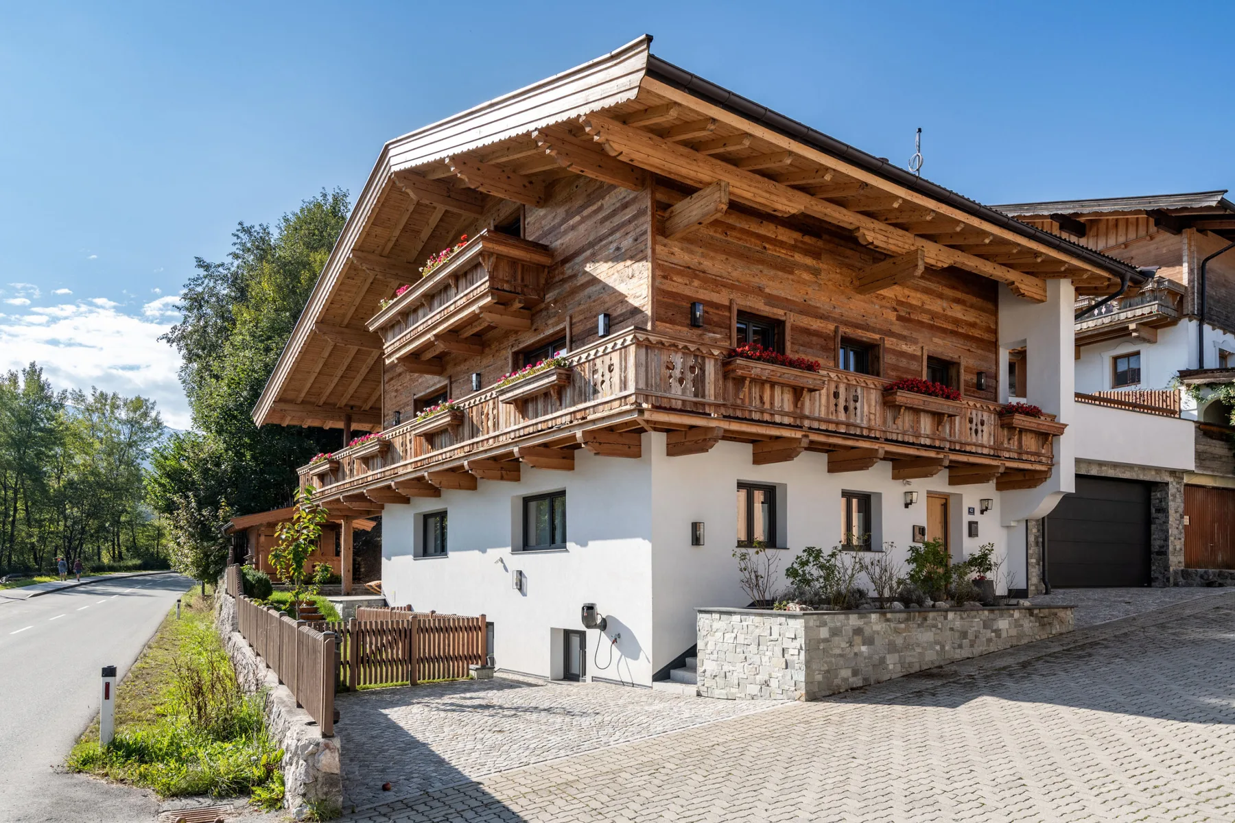 Una casa grande de estilo chalet con balcones de madera junto a una entrada pavimentada.