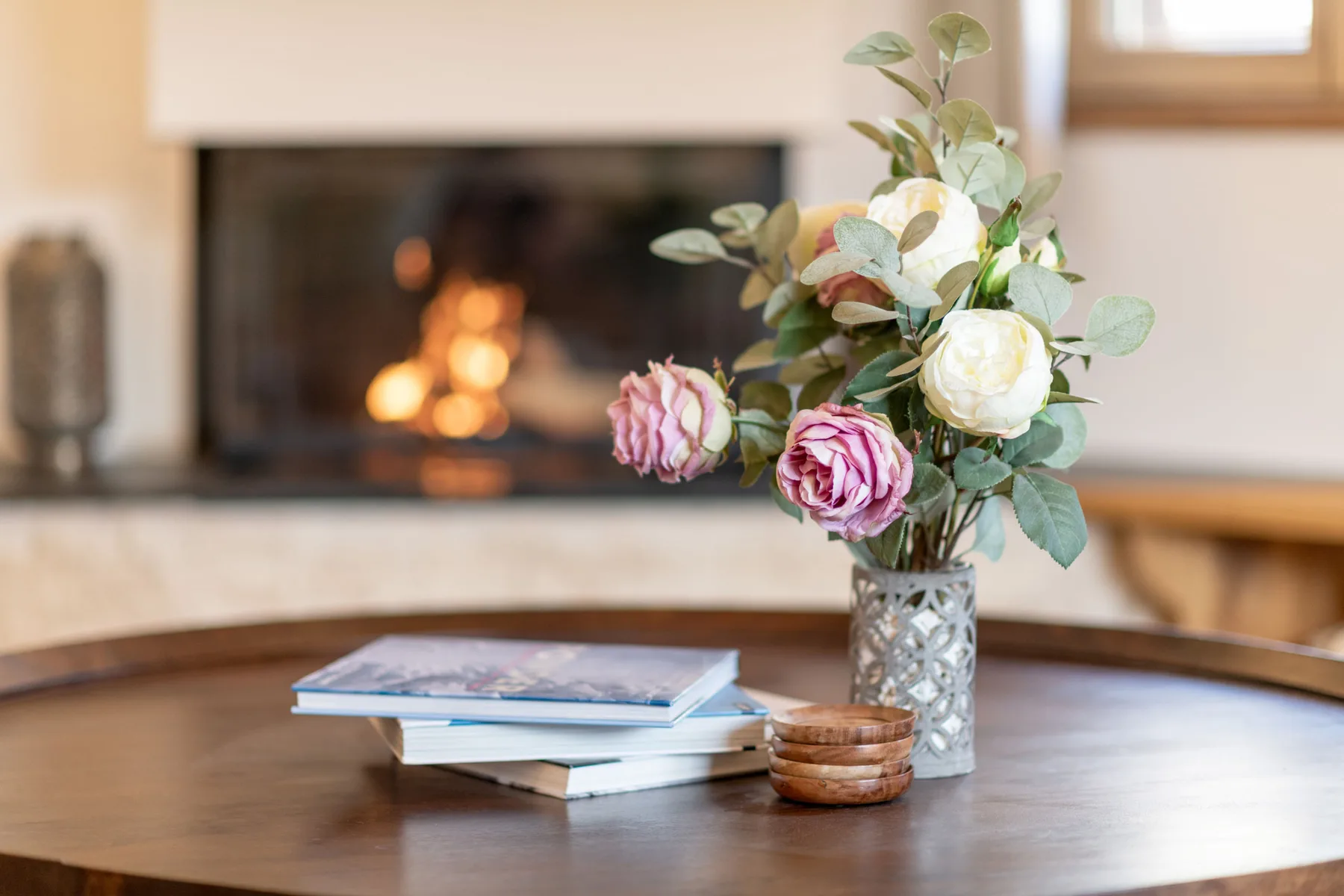 Un jarrón con flores y unos libros apilados están sobre una mesa frente a una chimenea.