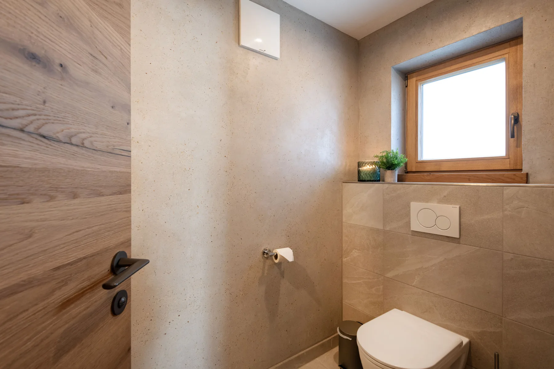 Un baño con un inodoro debajo de una ventana y una puerta de madera.