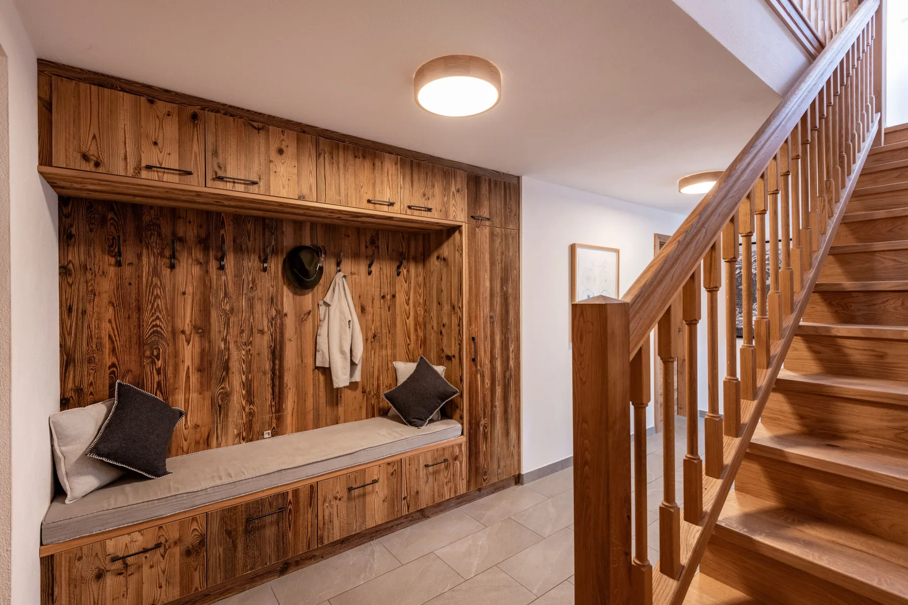 Un recibidor revestido de madera tiene un banco empotrado con percheros junto a una escalera.