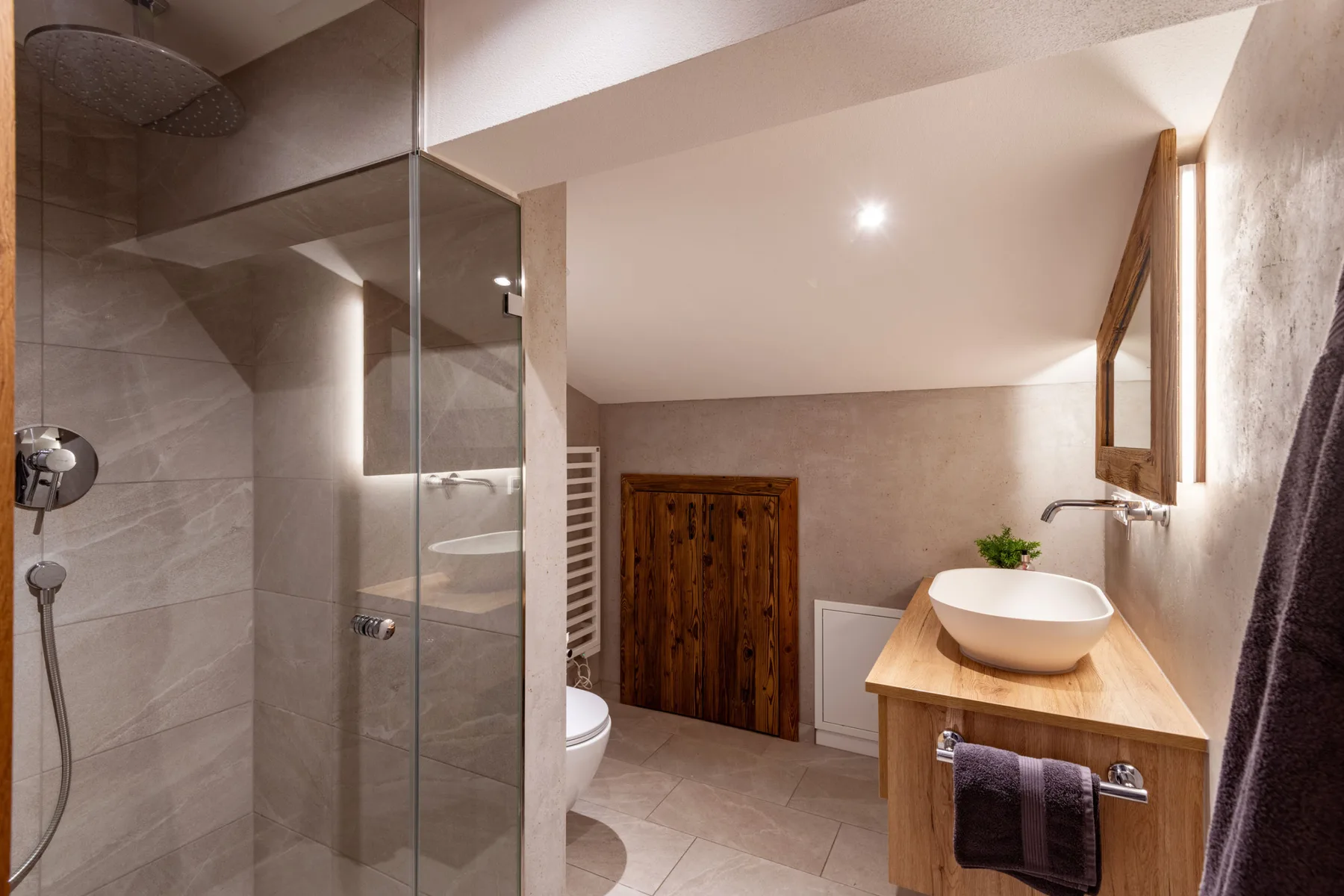 Un baño revestido de azulejos, con ducha de vidrio y mueble de madera.