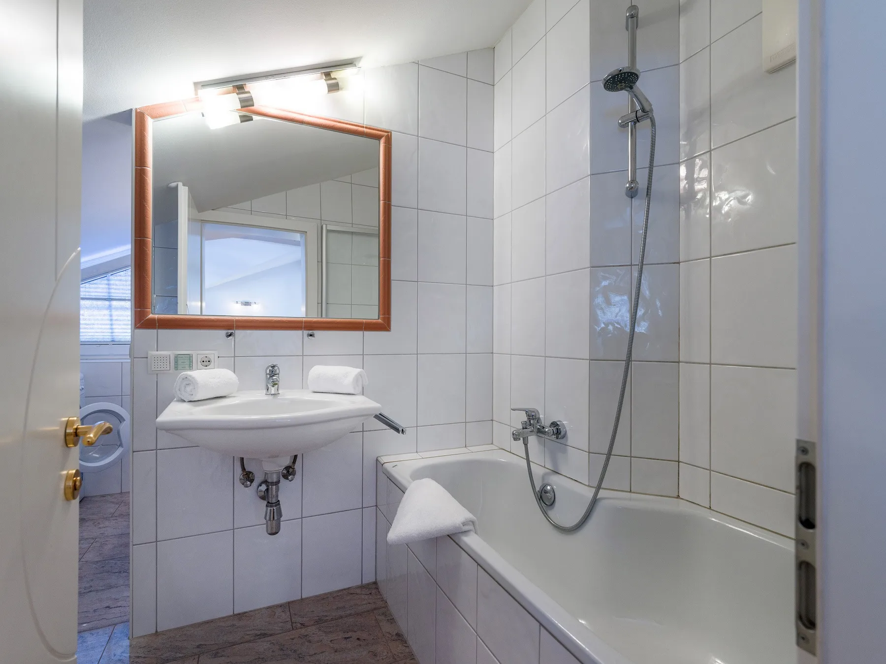Un baño alicatado con lavabo, espejo y bañera con ducha.