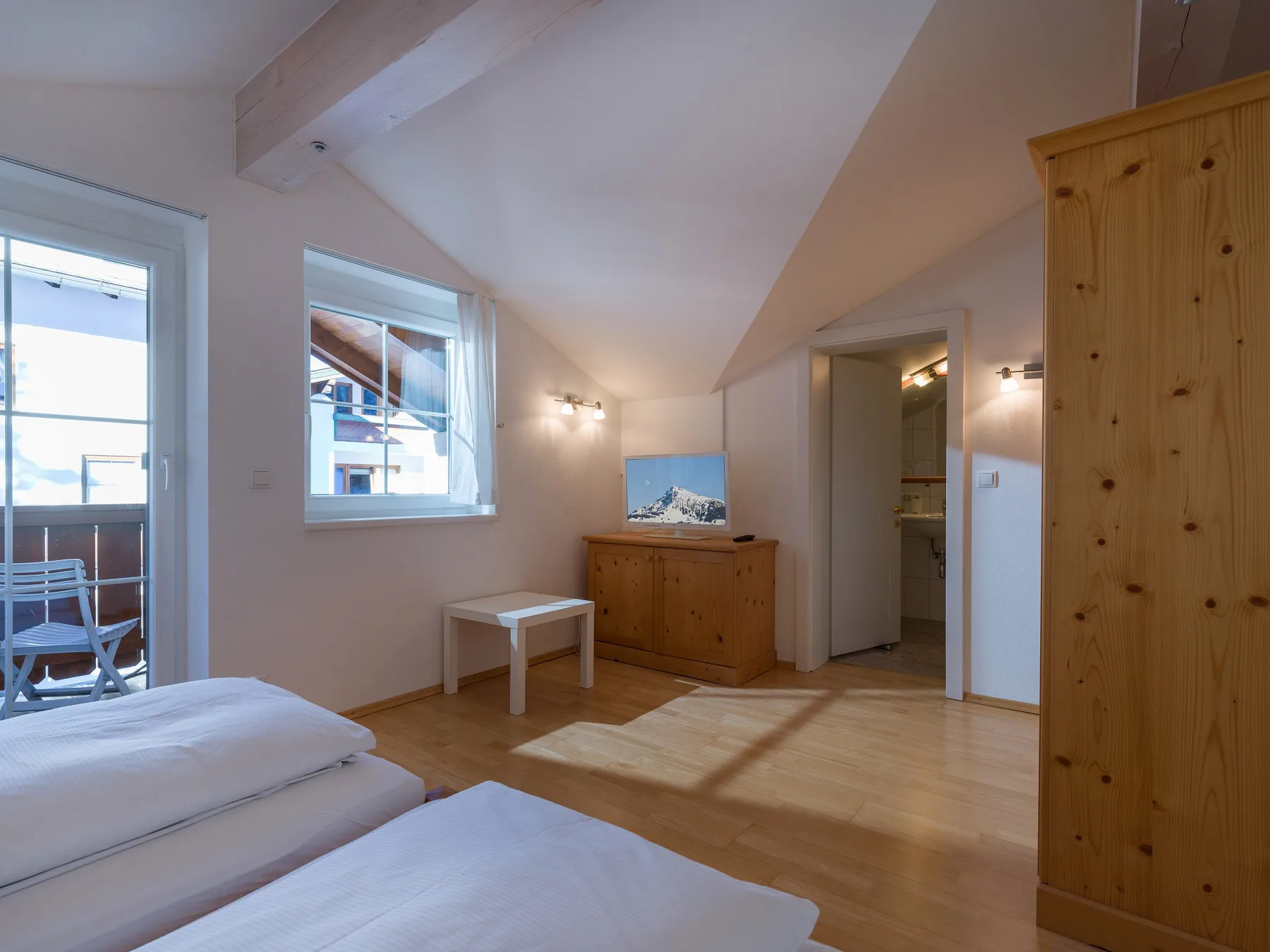 Un dormitorio luminoso con techo inclinado, una cama y una cómoda de madera.