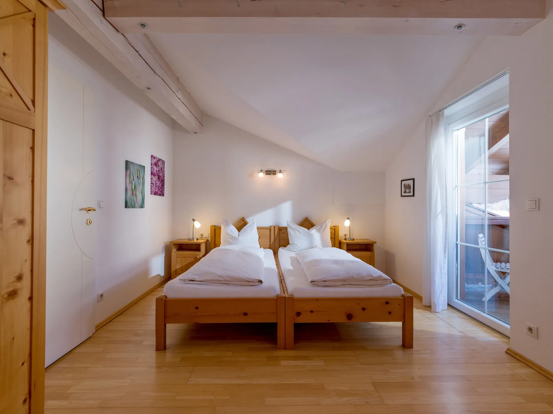 Un dormitorio abuhardillado y luminoso con dos camas y una puerta acristalada que da a un balcón.