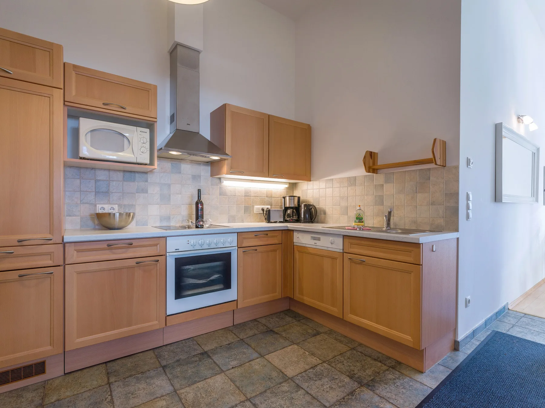 Una cocina con armarios de madera, horno empotrado y suelo de baldosas.