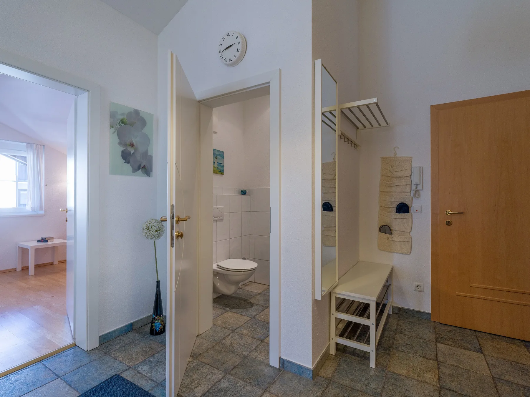 Un pasillo interior con puertas abiertas, suelo de baldosas y un reloj de pared.