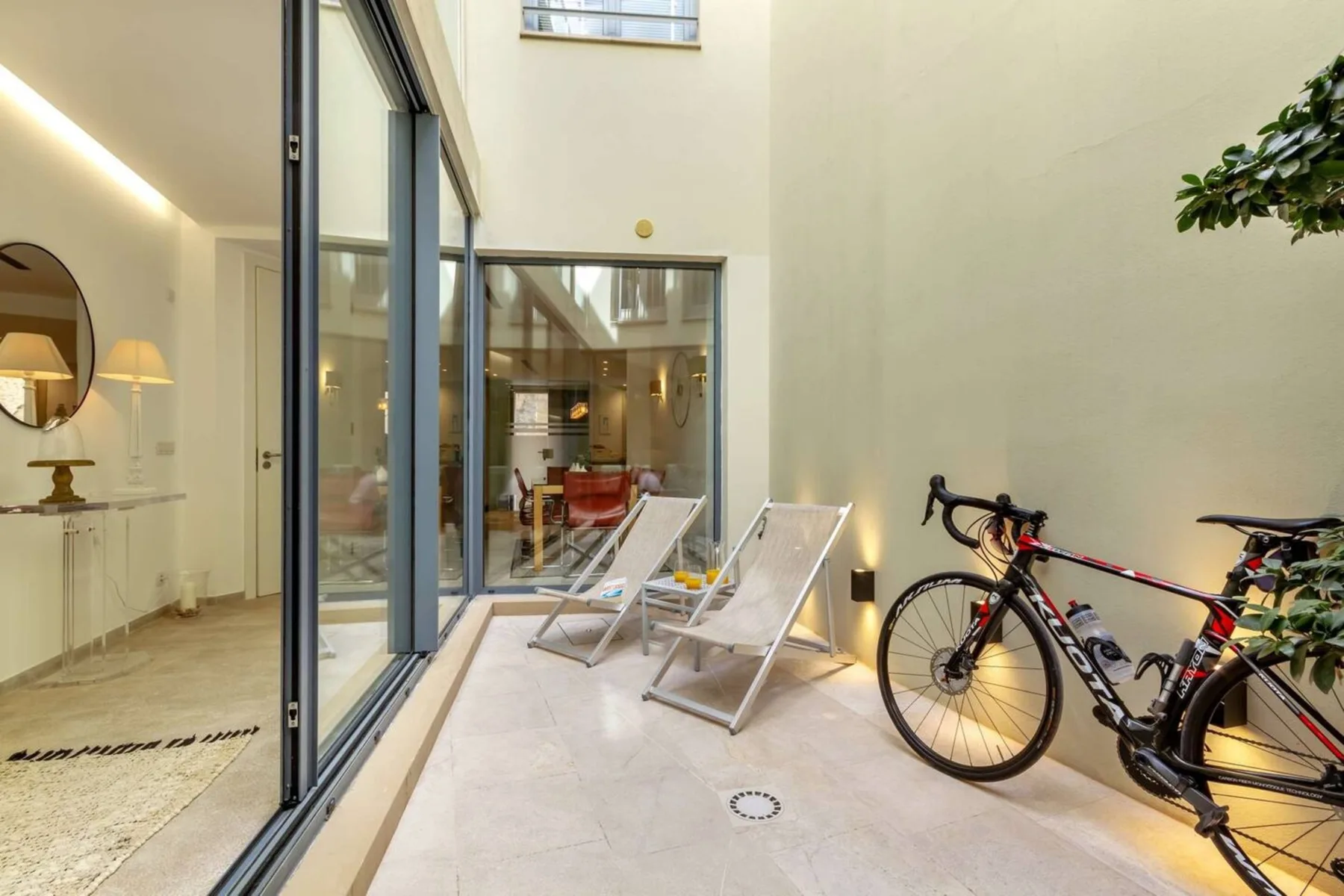 Un patio interior luminoso con sillas reclinables, bicicletas y puertas de vidrio.