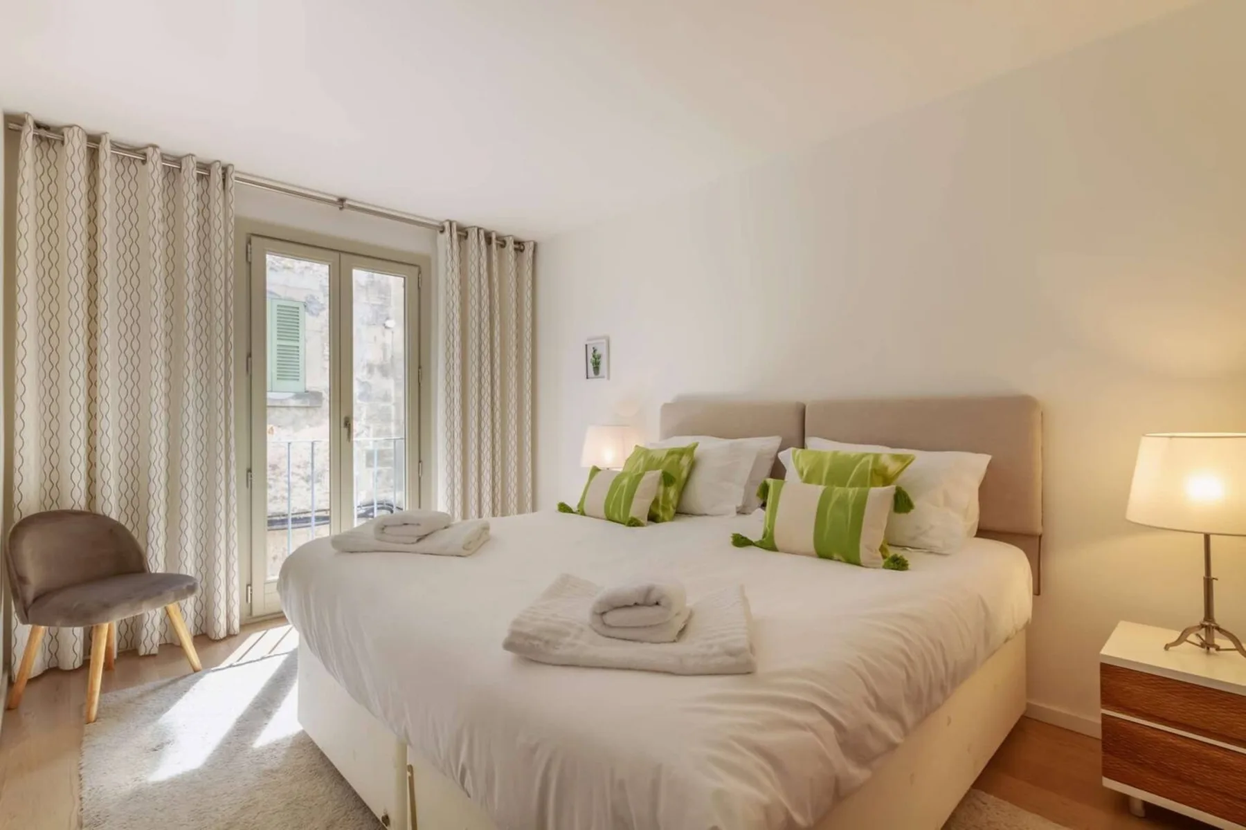Un dormitorio luminoso con una cama bien tendida y cortinas junto a las puertas de cristal.