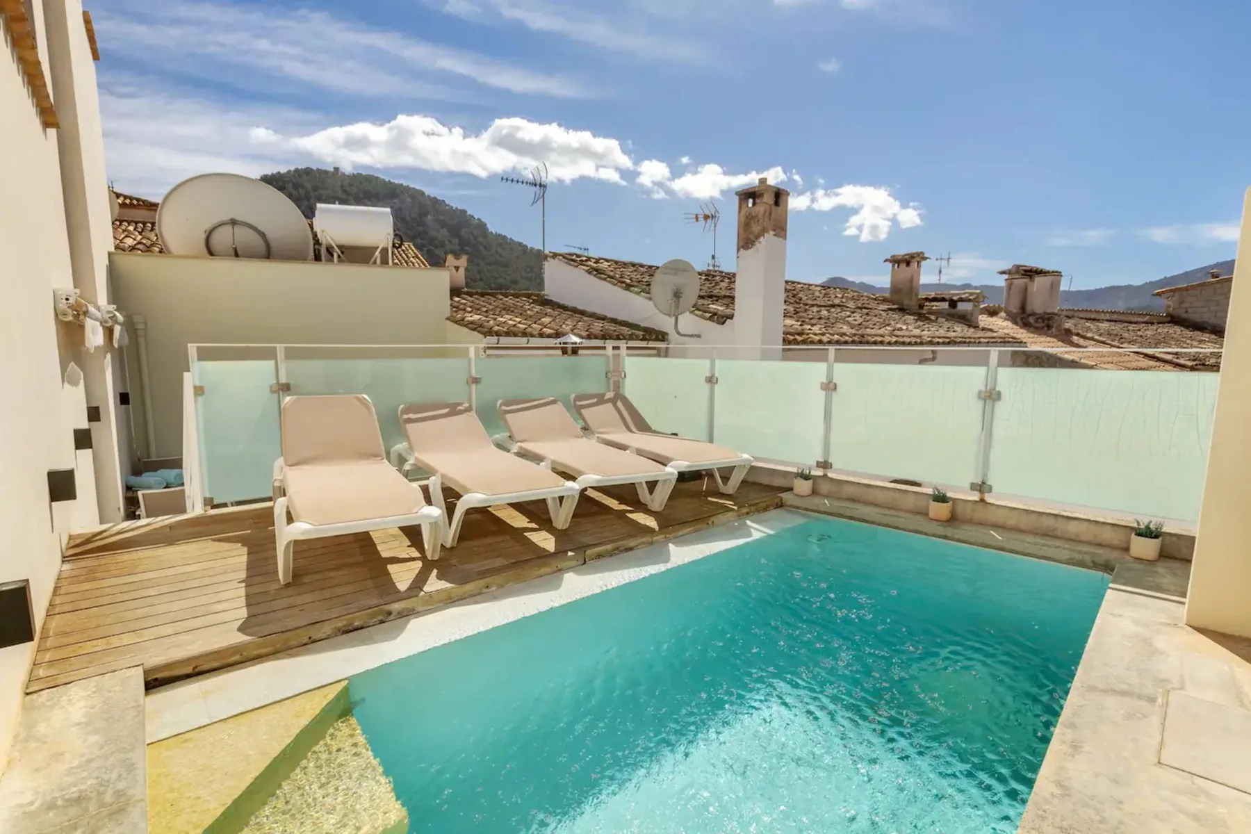 Una zona de piscina en la azotea con tumbonas junto a barandillas de vidrio.