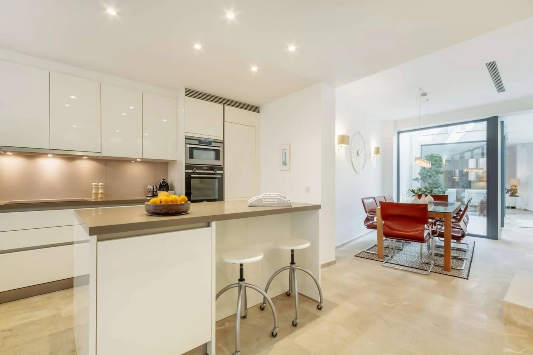 Cocina y comedor diáfanos y luminosos, con una isla central y puertas de vidrio.