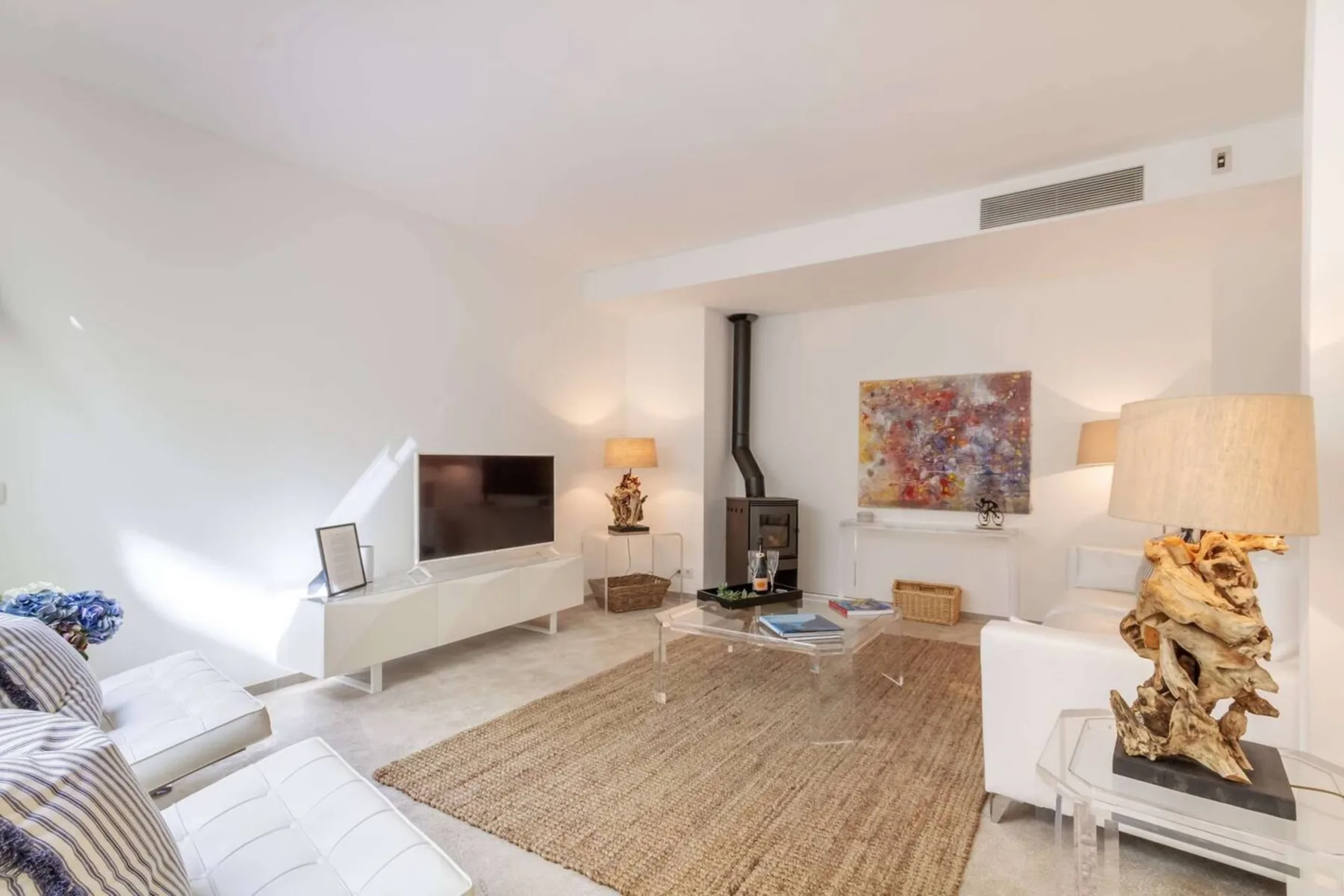 Una sala luminosa con asientos blancos, un televisor y una estufa de leña.