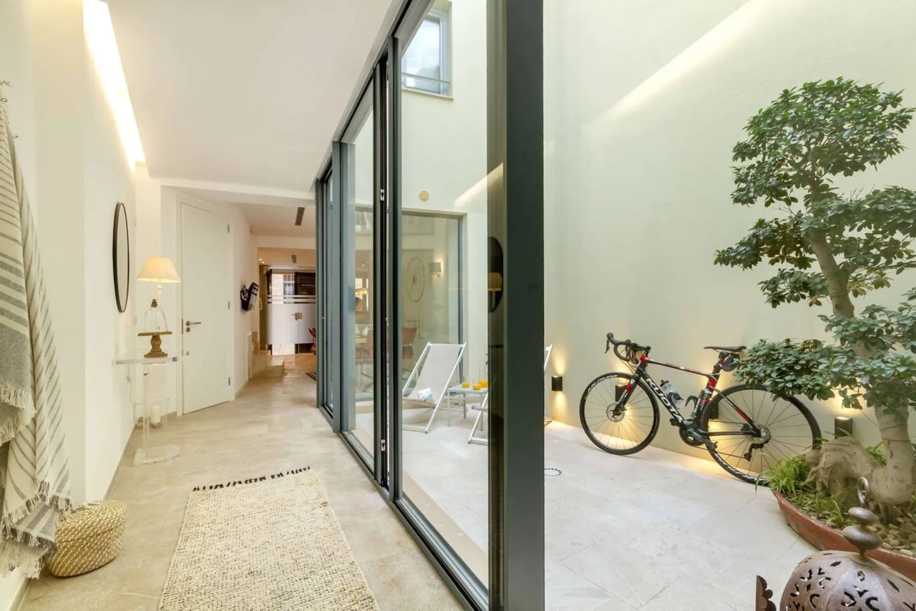 Un pasillo luminoso da a un patio acristalado con una bicicleta y un árbol en maceta.