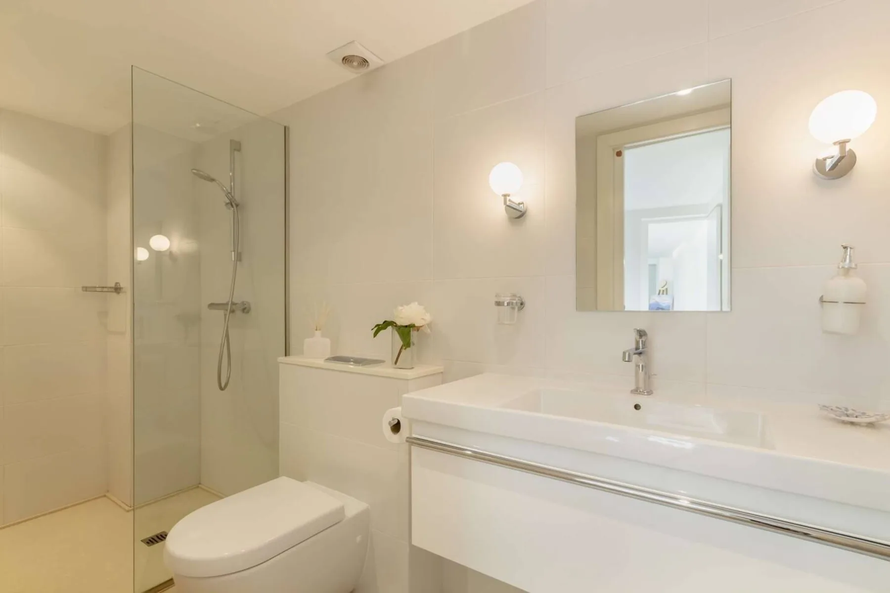 Un baño luminoso con ducha de vidrio, inodoro y lavabo blanco.