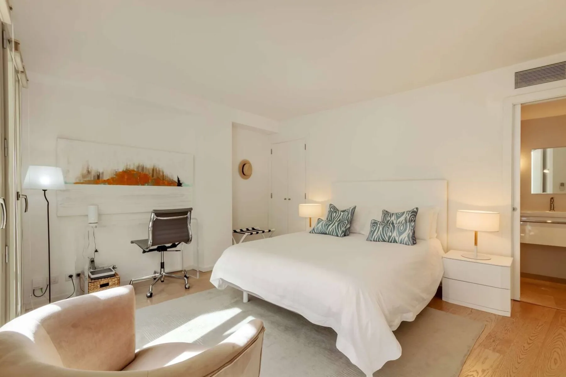 Un dormitorio luminoso con una cama tendida y un escritorio junto a la ventana.