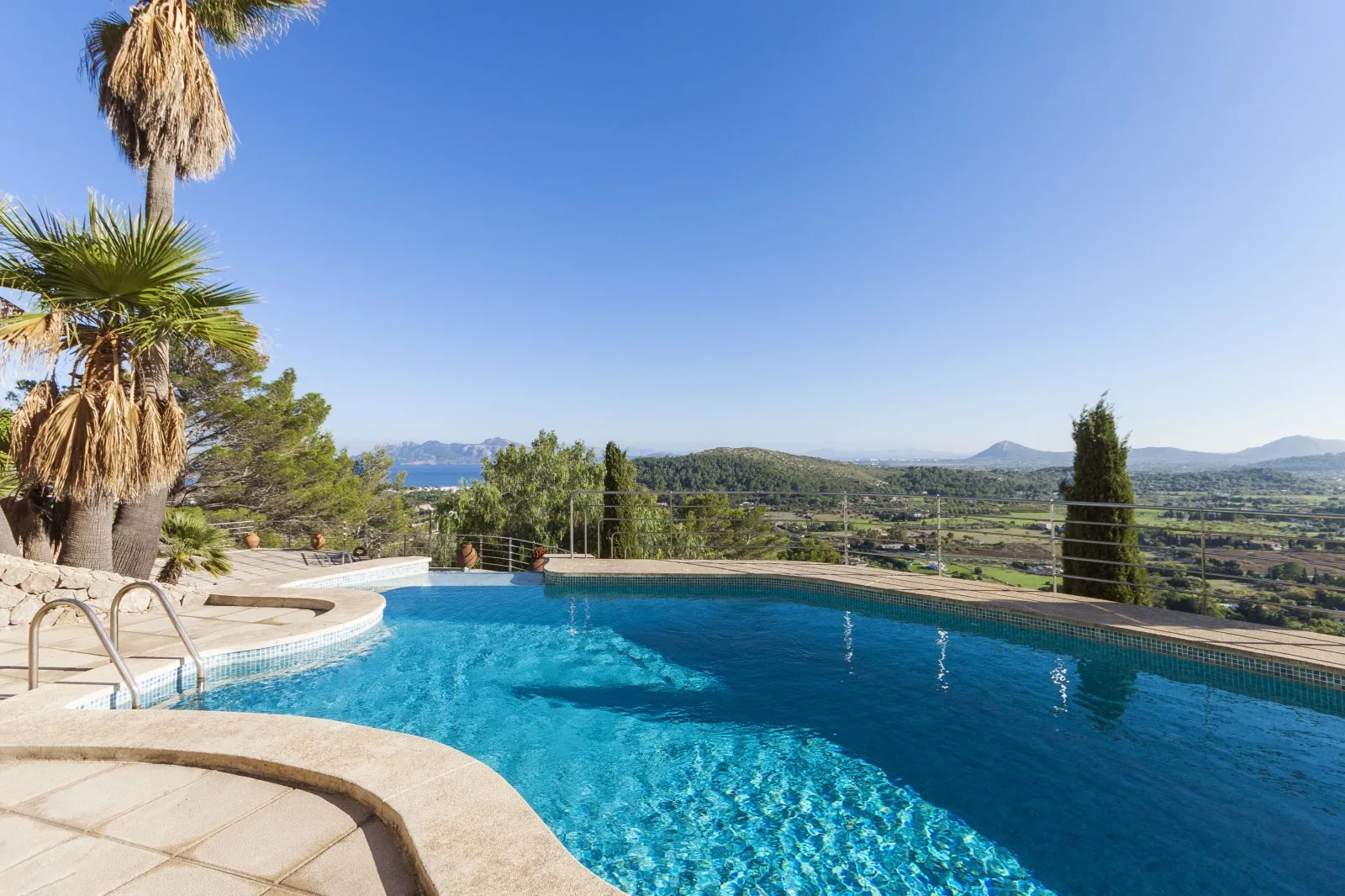 An outdoor swimming pool overlooks a green valley and distant hills.