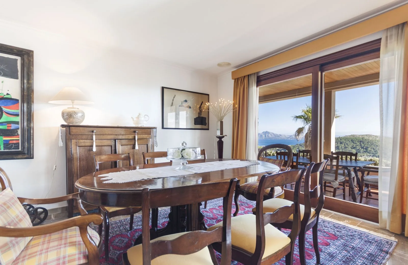A dining room with a large table beside windows overlooking a coastal view.