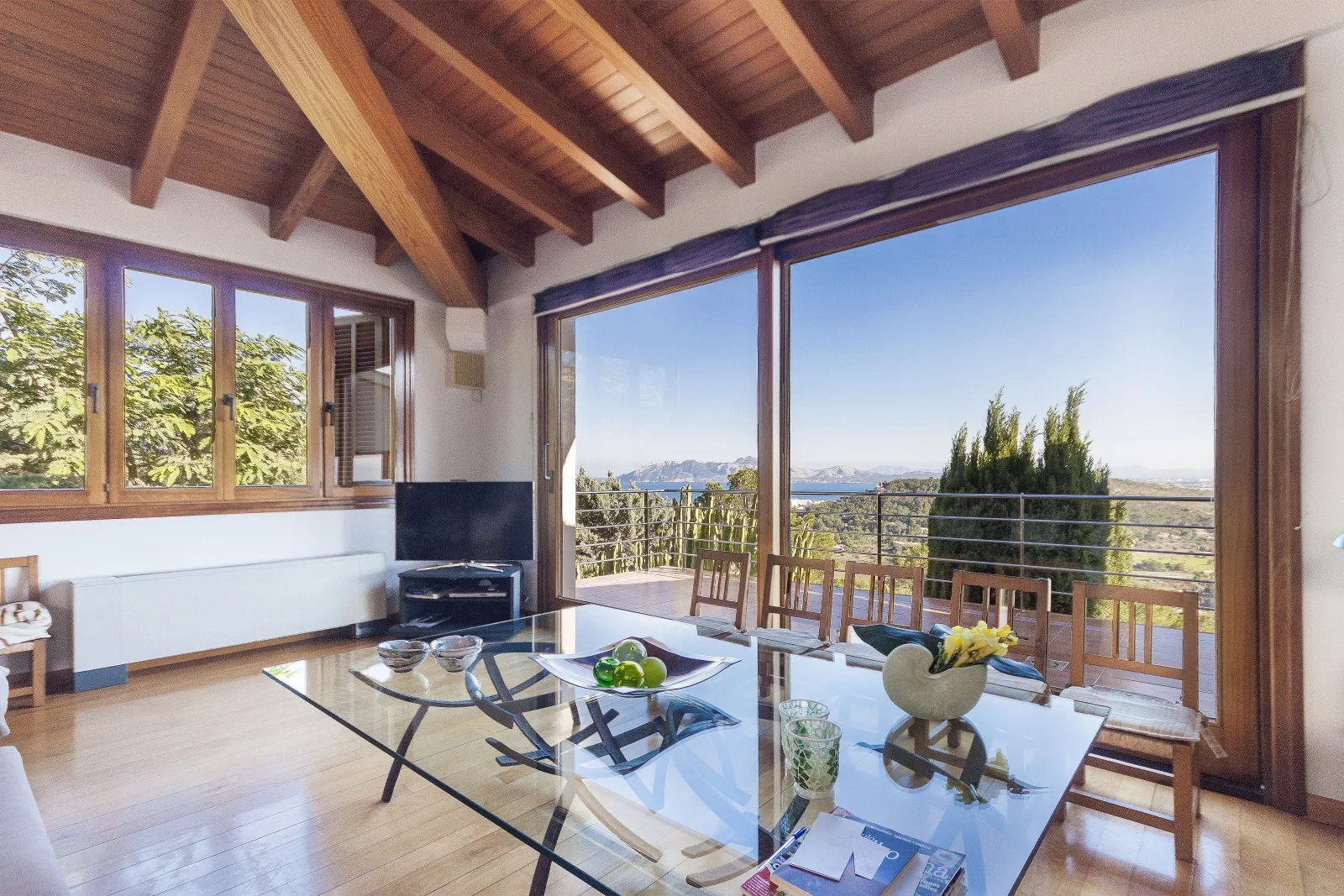 A bright living room with a glass dining table and wide windows overlooking the landscape.