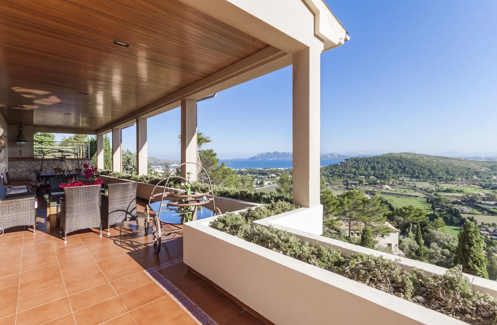 A covered outdoor dining terrace overlooks green hills and the sea.