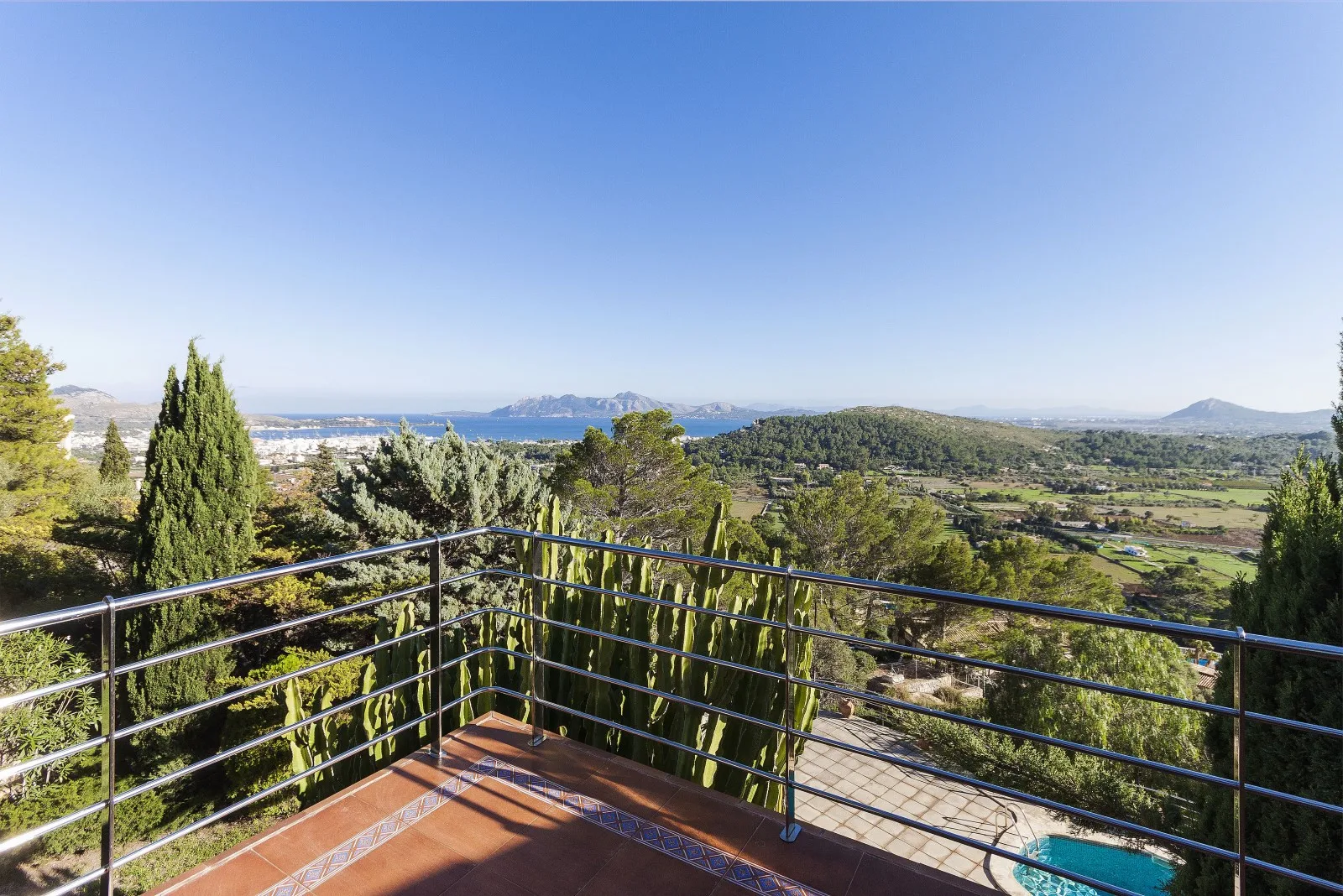 A balcony overlooks a green landscape with distant hills and a small pool below.