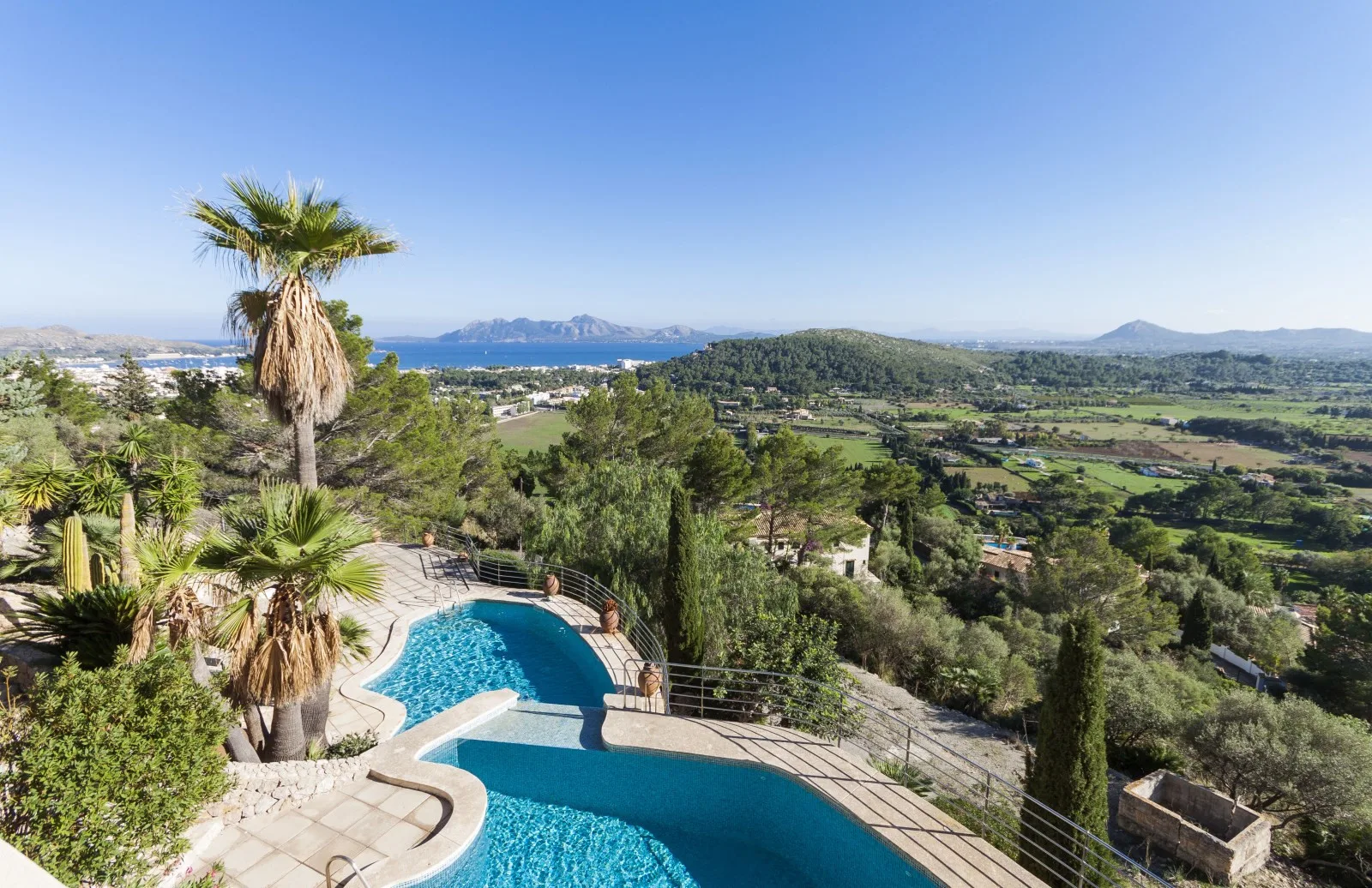 A curved outdoor swimming pool overlooks a green valley and distant hills.