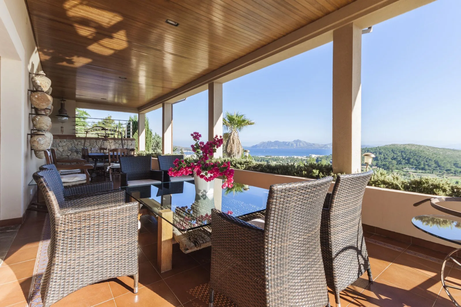 A covered terrace with wicker seating overlooks a pool and distant hills.