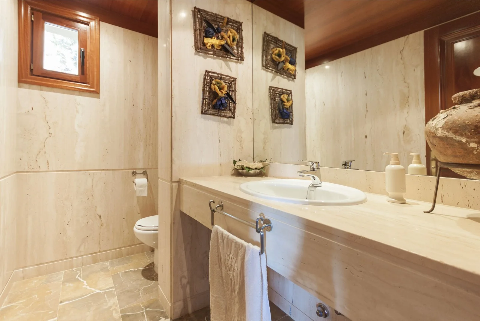A bathroom with a long vanity, sink, and toilet beside a small window.