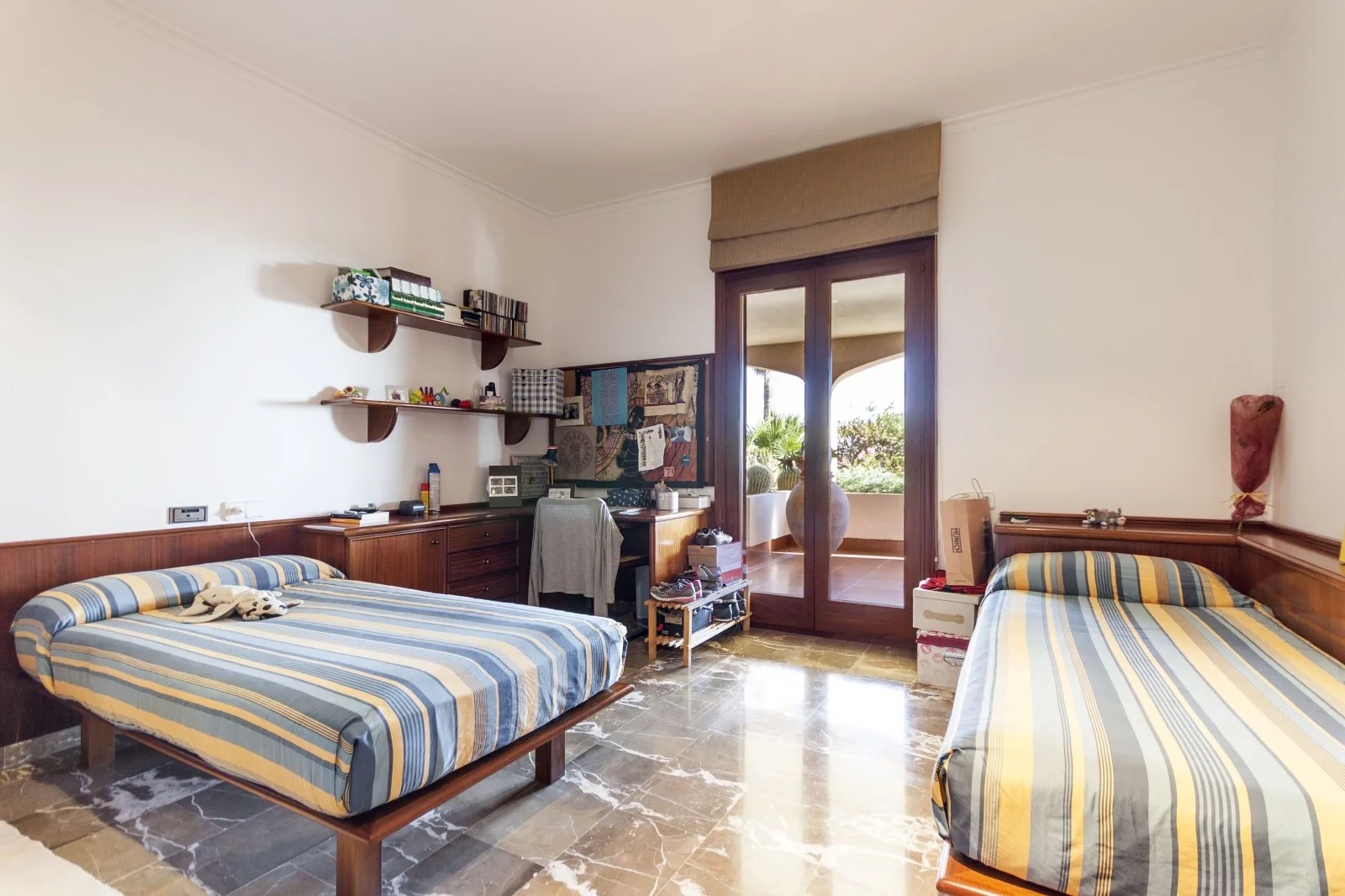 A bedroom with two beds and glass doors opening onto a balcony.