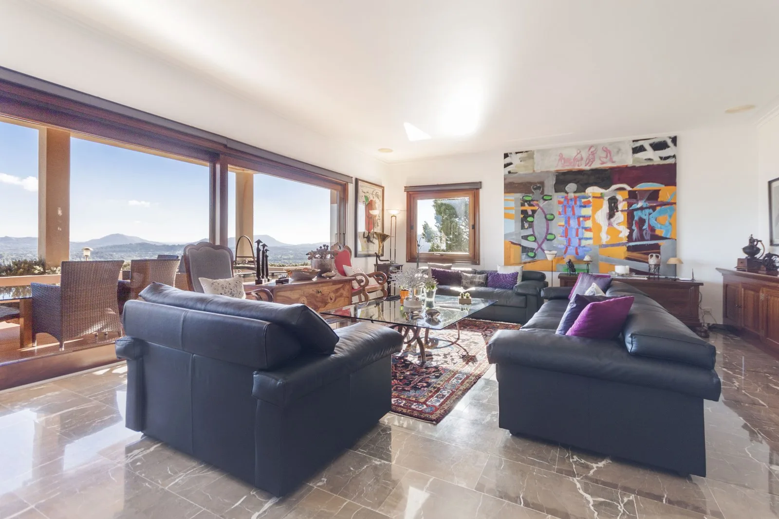 A bright living room with dark seating, large windows, and colorful wall art.