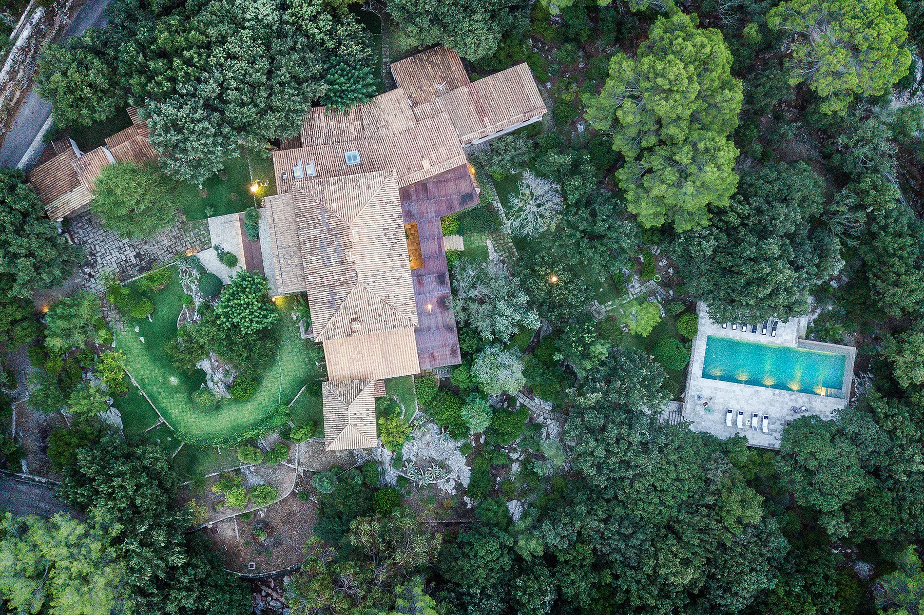 An aerial view of a tiled-roof building and swimming pool surrounded by trees.