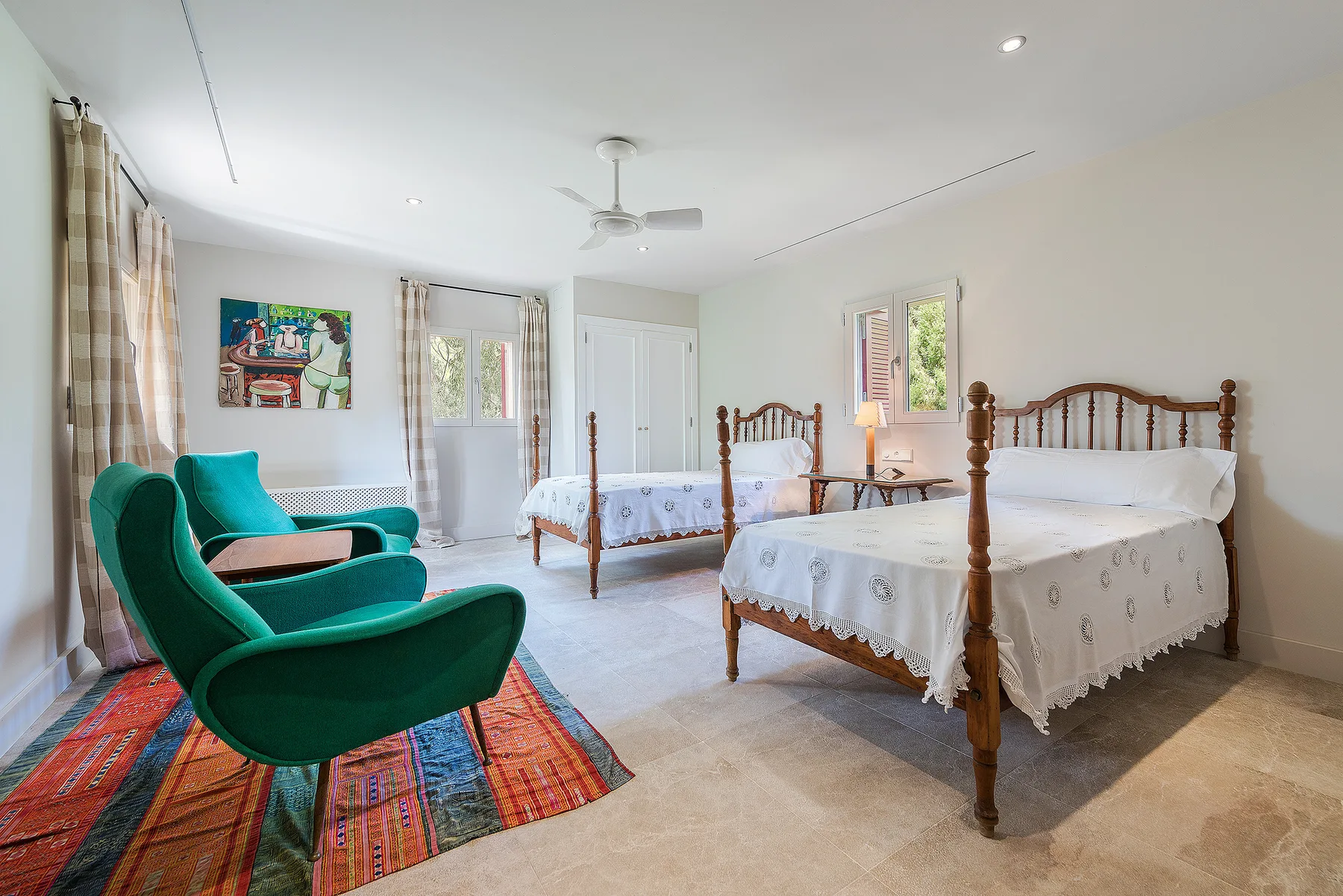 A bright bedroom with two beds, teal seating, and colorful rugs.