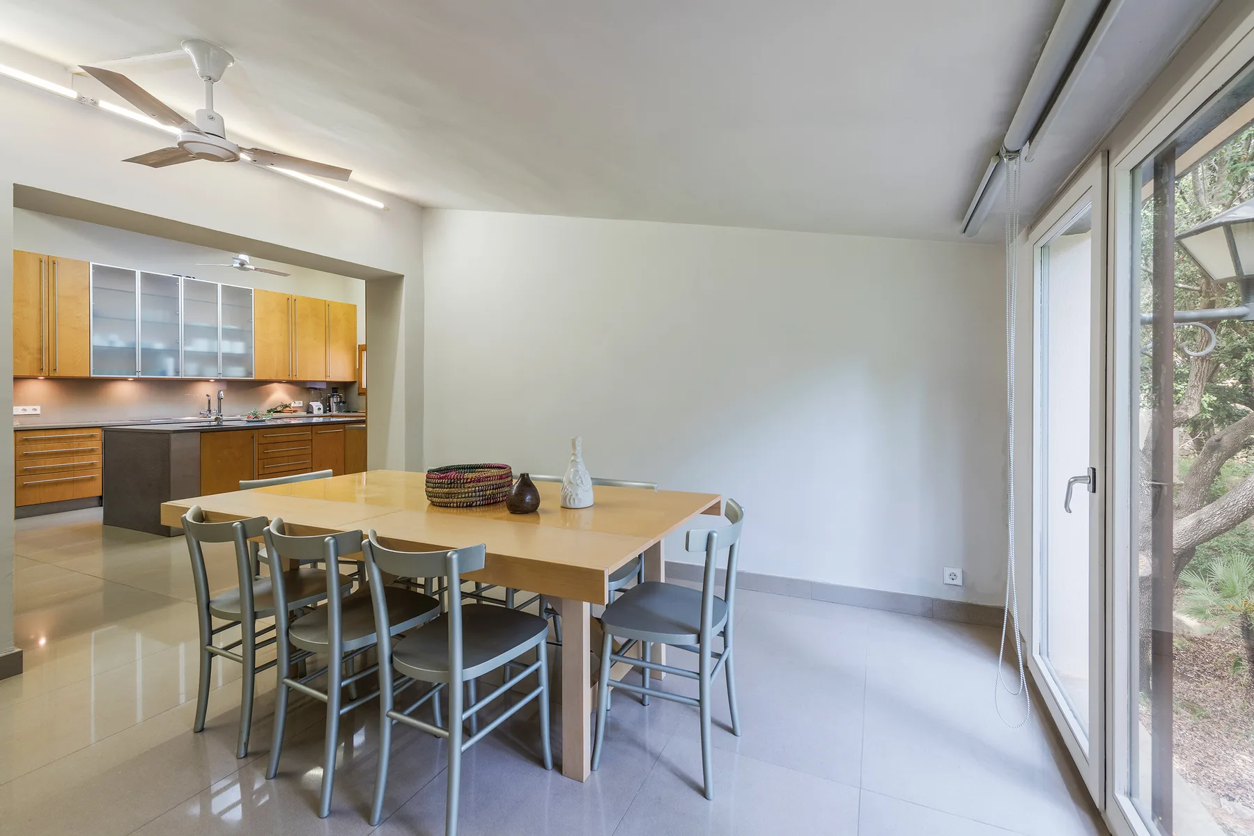 A dining area with a wooden table beside an open kitchen and large windows.
