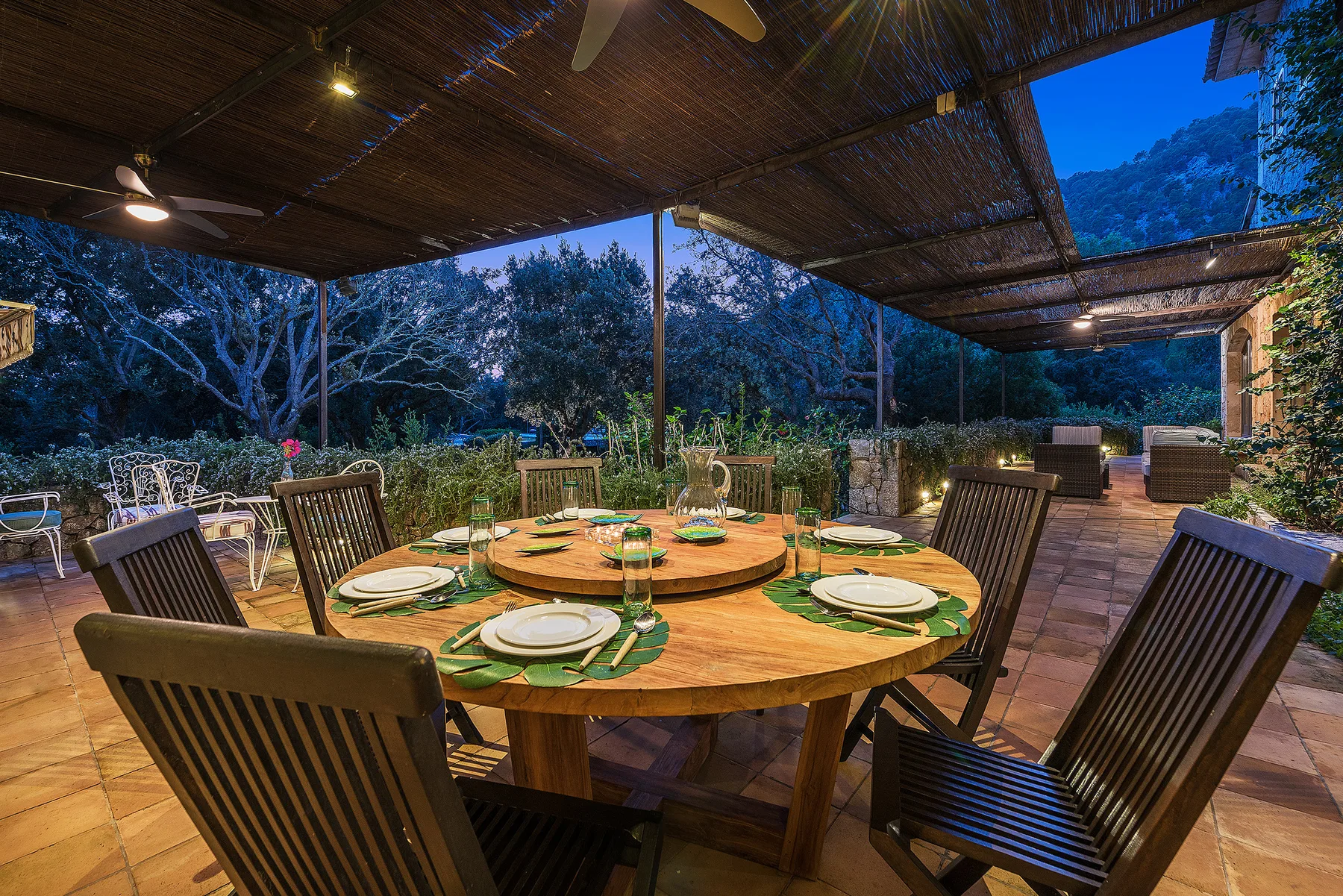An outdoor dining area under a shaded canopy, with a set table overlooking trees.
