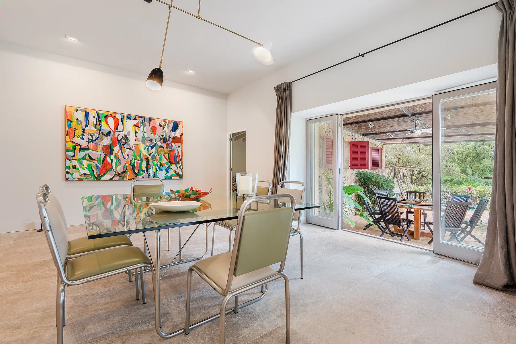 A dining area with a glass table and colorful artwork on the wall.