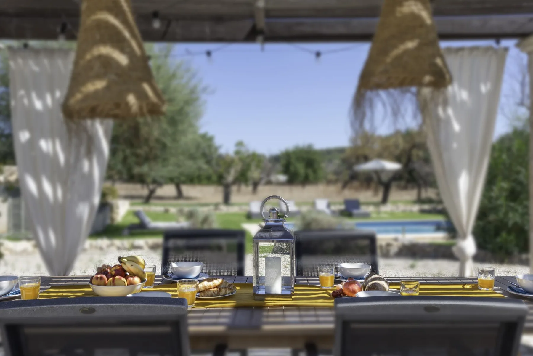 Una mesa de comedor al aire libre está servida bajo lámparas tejidas colgantes.