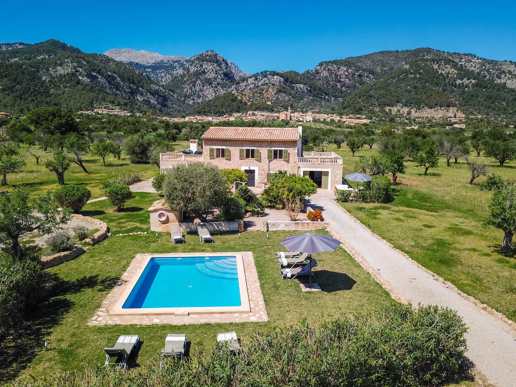 Una casa rural con piscina se encuentra entre campos verdes, bajo las montañas.