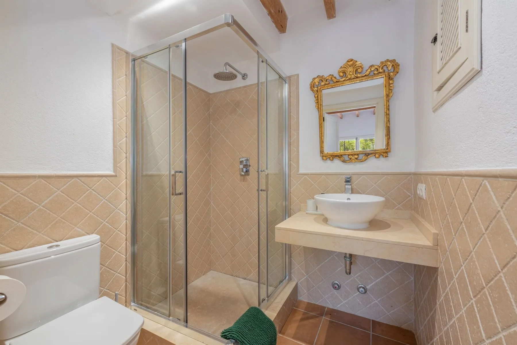 Un baño con azulejos, una ducha de vidrio y un lavabo bajo un espejo ornamentado.