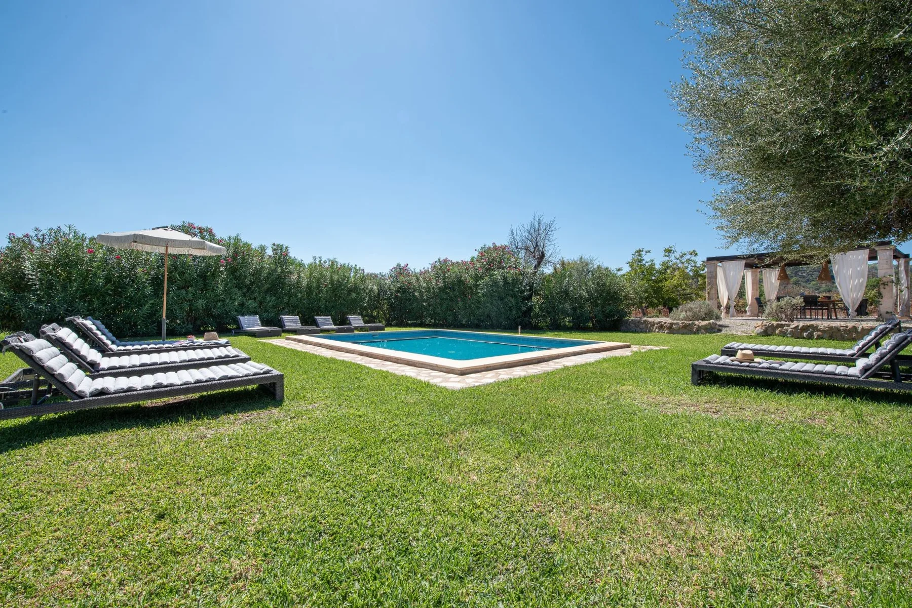 Una piscina al aire libre está en un jardín con césped y tumbonas cerca.
