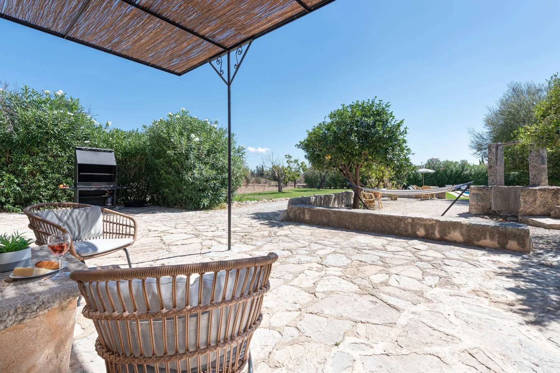 Un patio exterior de piedra con asientos, una cubierta de sombra y un jardín.