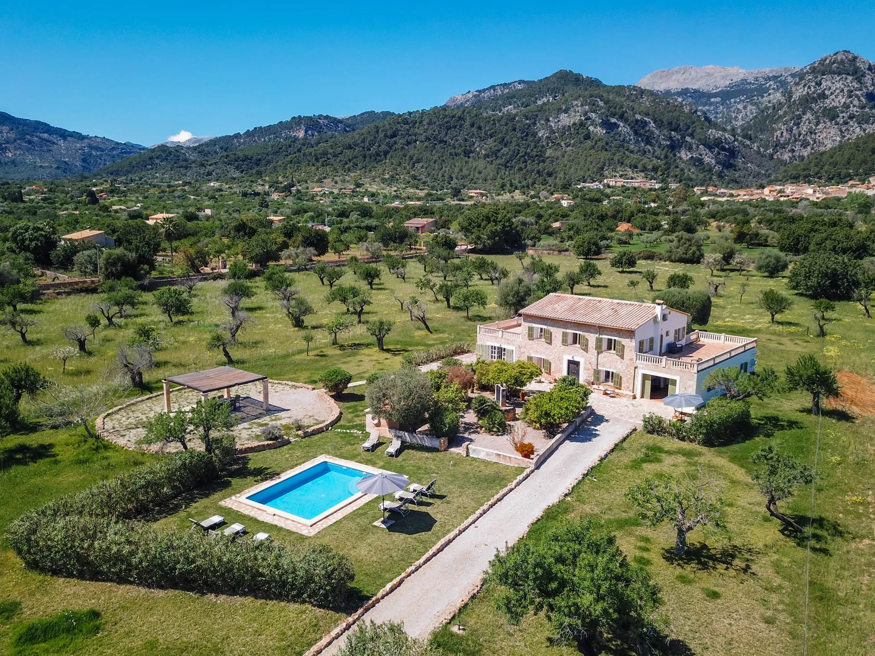 Una casa rural está junto a una piscina, rodeada de campos verdes y montañas.