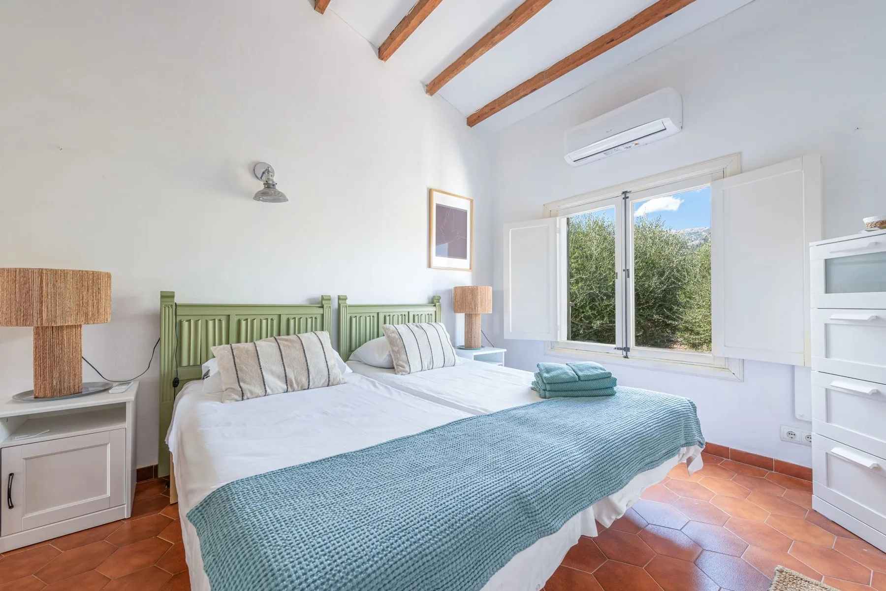 Un dormitorio luminoso con una cama, cabecero verde y ventana abierta.