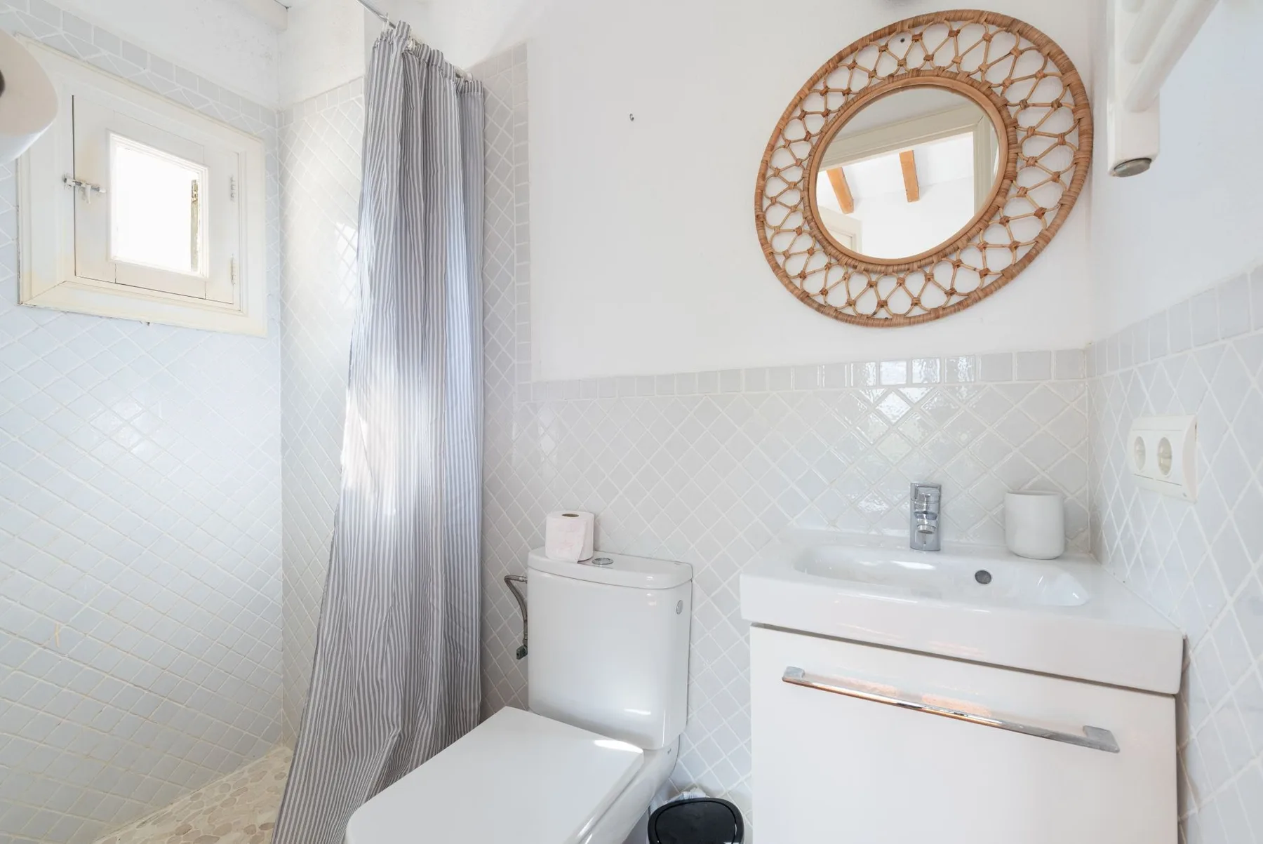 Un baño luminoso con inodoro, lavabo y espejo decorativo.