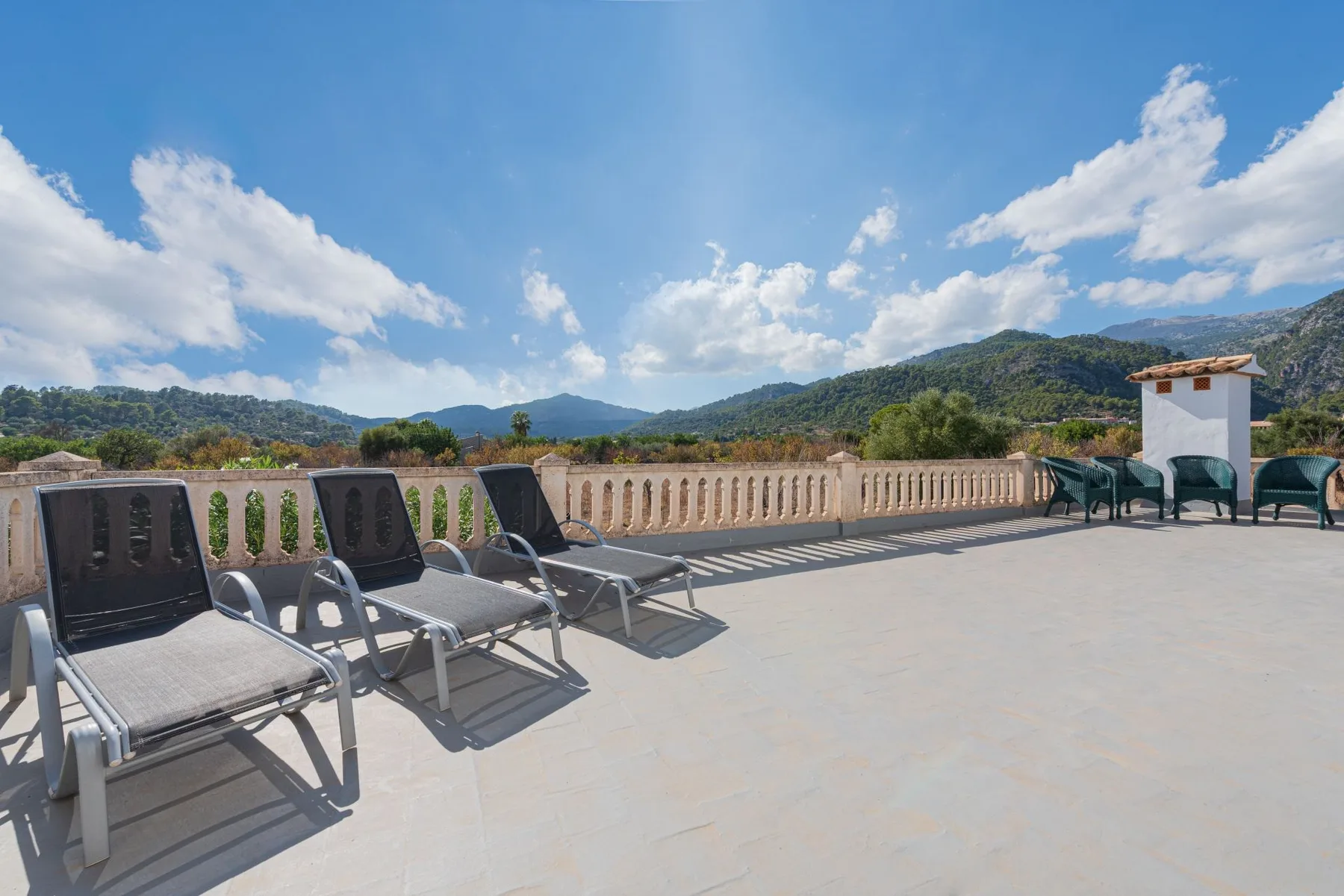 Una terraza soleada con asientos reclinables ofrece vistas a colinas verdes bajo un cielo azul.