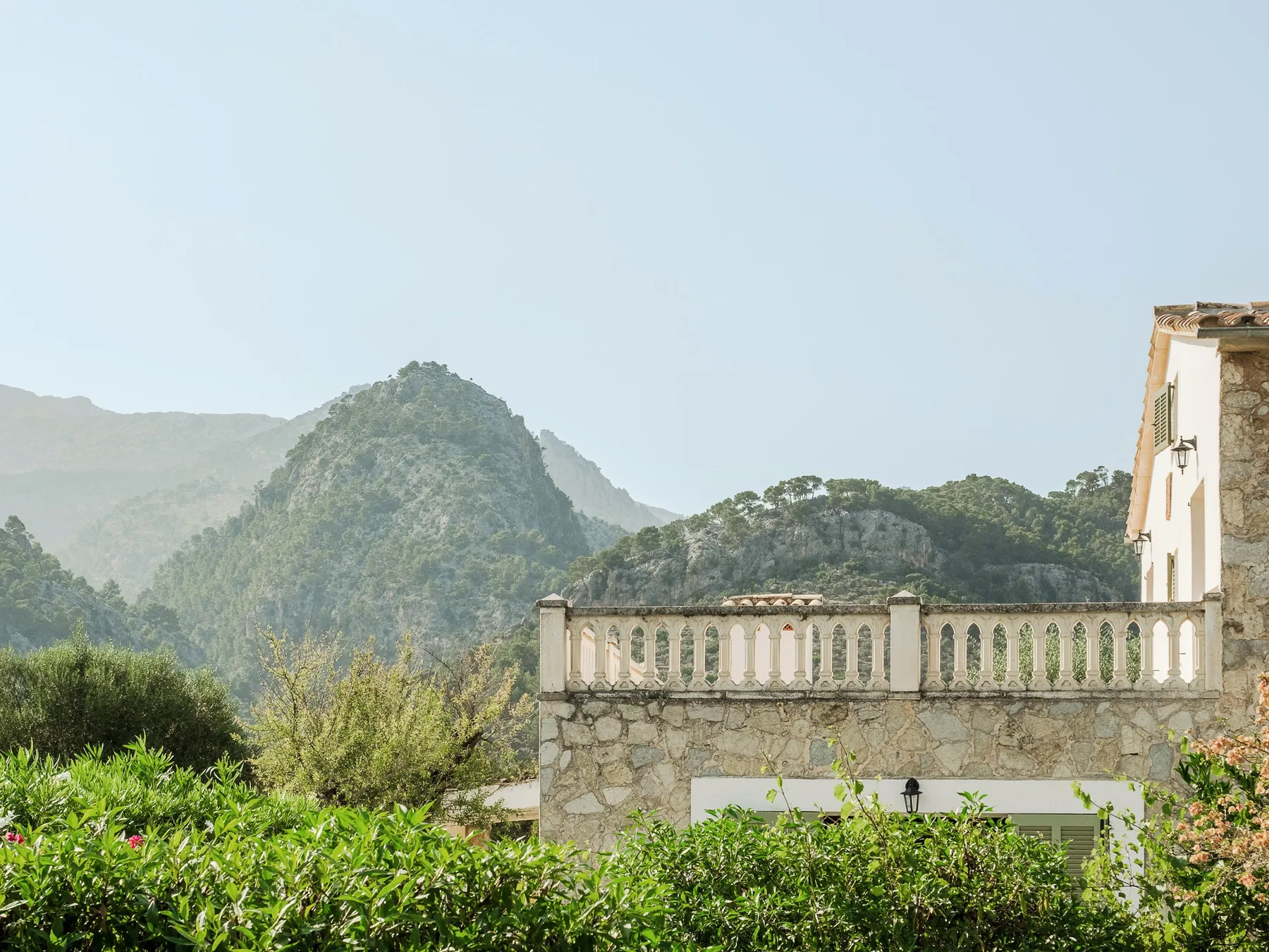 Una terraza de piedra da a un jardín verde y un paisaje montañoso.