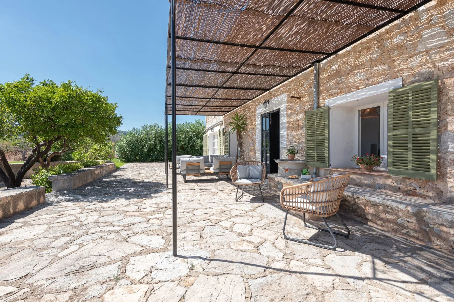 Un patio de piedra con asientos al aire libre está bajo un toldo de cañizo.